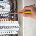 A person using an insulated screwdriver to adjust wiring inside an electrical distribution board