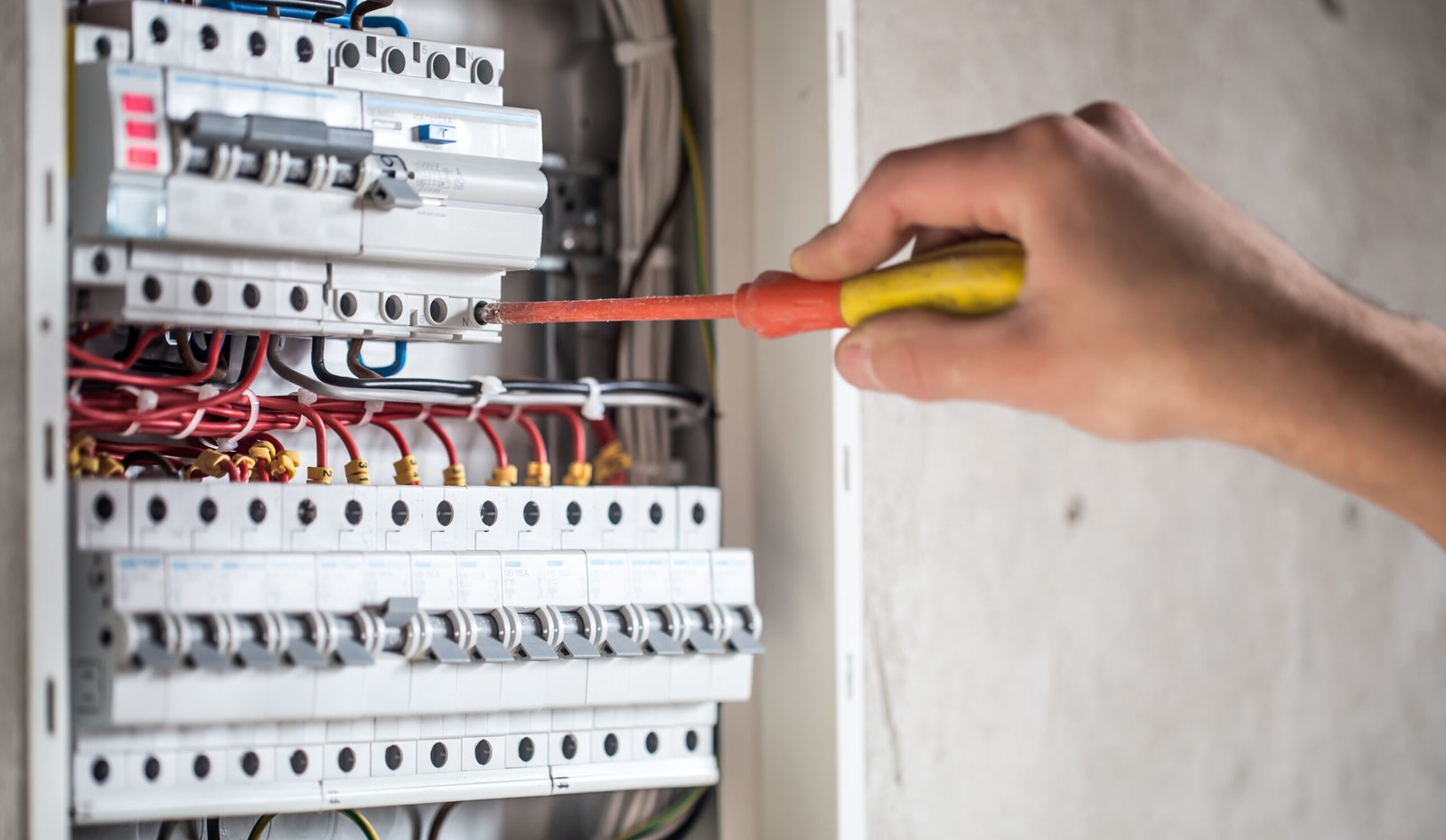 A person using an insulated screwdriver to adjust wiring inside an electrical distribution board